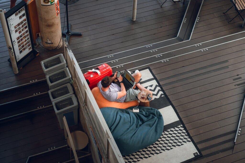 Person working on a laptop beside luggage at a café in Bangkok