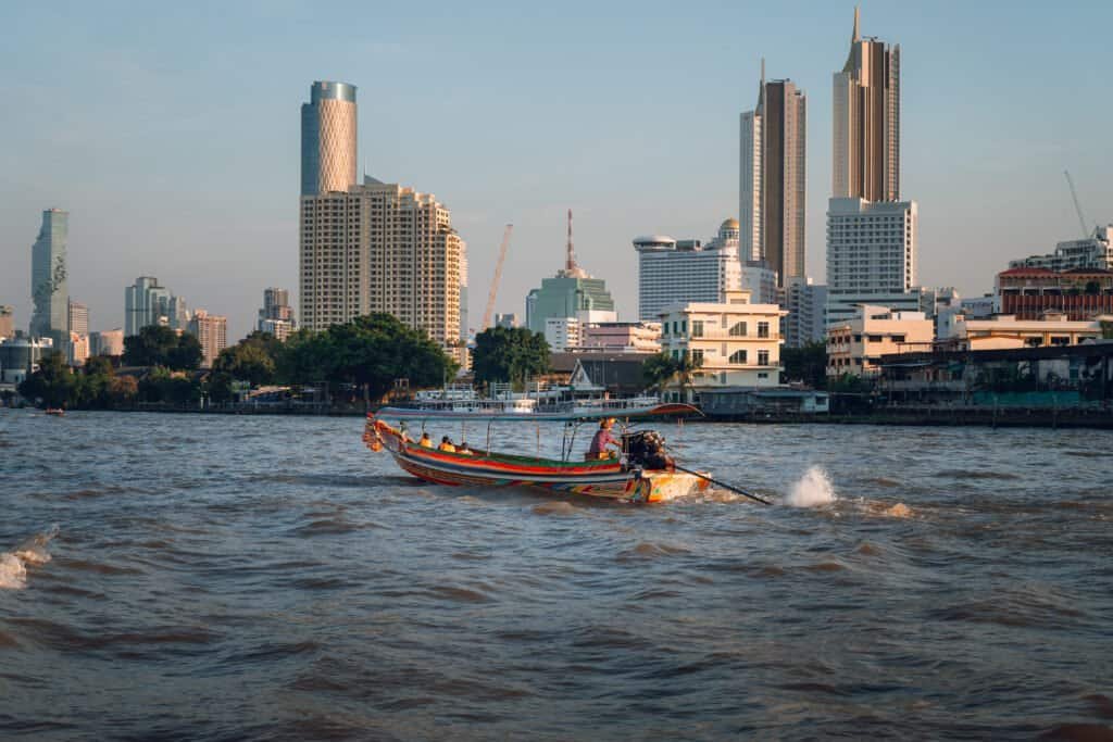 Longtail boat traveling on the Chao Phraya River with Bangkok skyline behind it