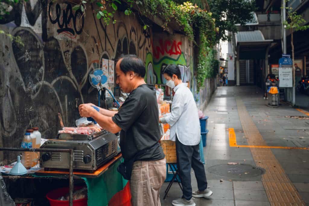 Street food vendors preparing food along a narrow alley in Bangkok