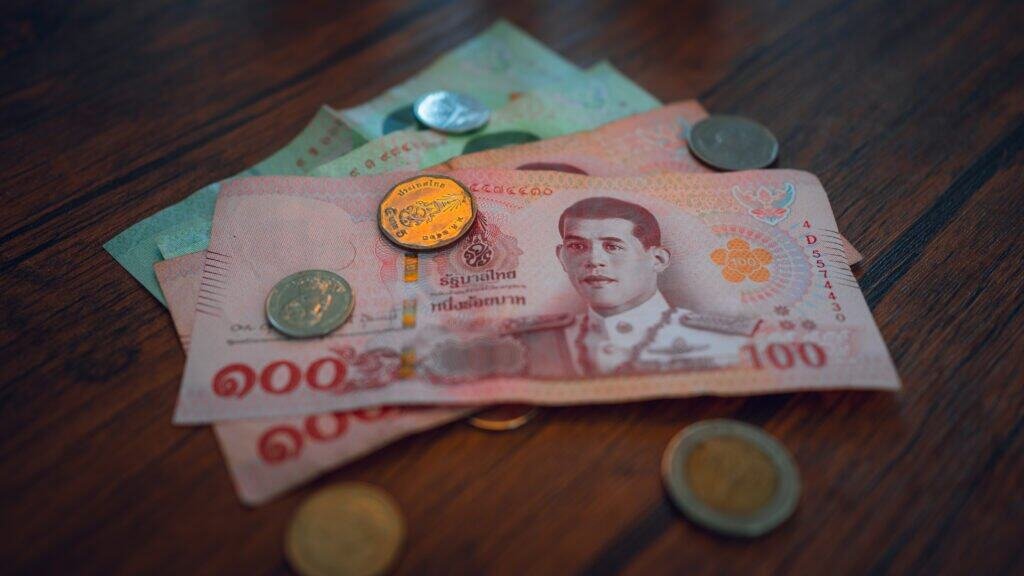 Thai baht banknotes and coins laid out on a wooden surface
