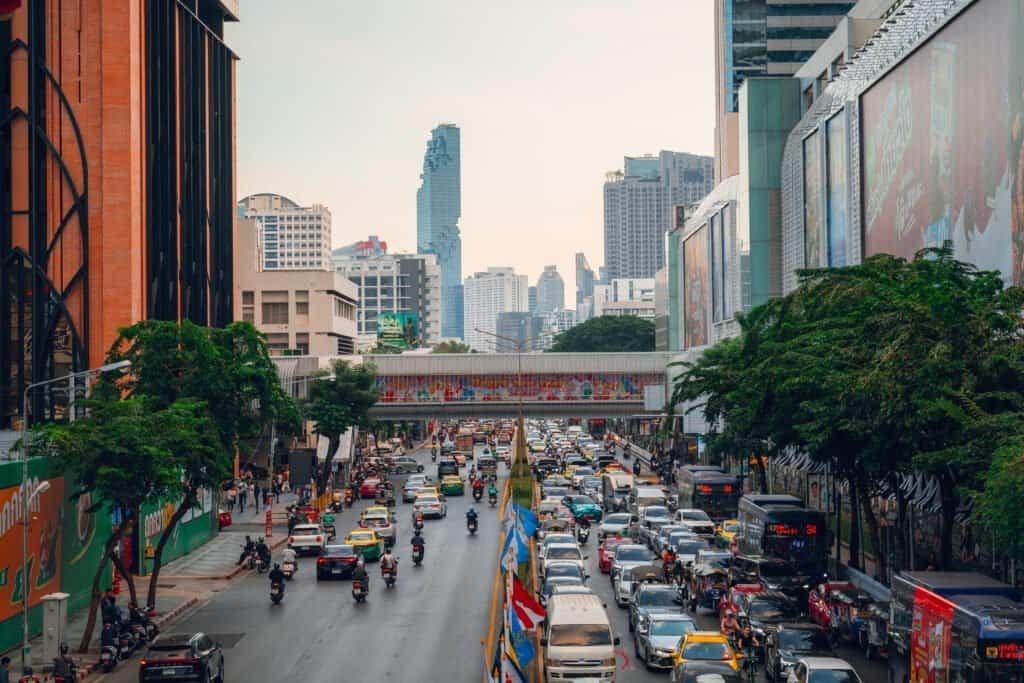 Busy traffic moving through a major Bangkok intersection beneath a pedestrian overpass