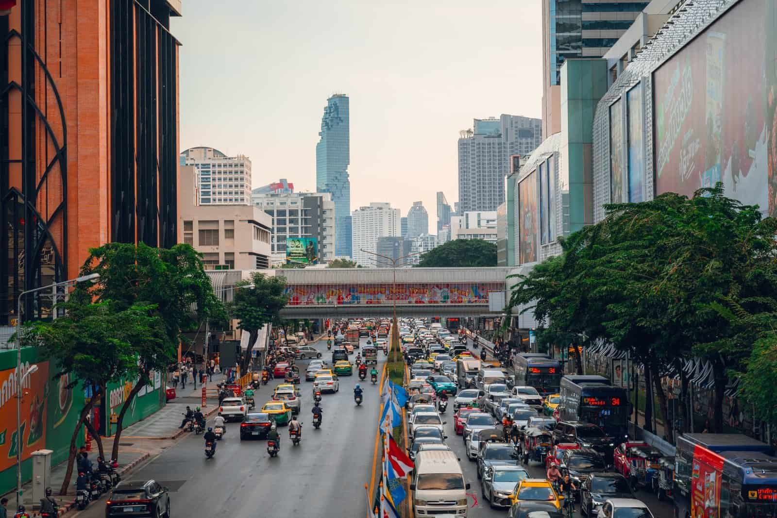 Busy traffic moving through a major Bangkok intersection beneath a pedestrian overpass